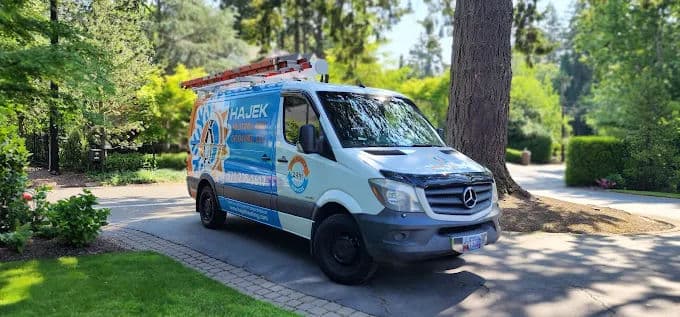 Hajek service van parked in a lush green yard with trees and landscaping.
