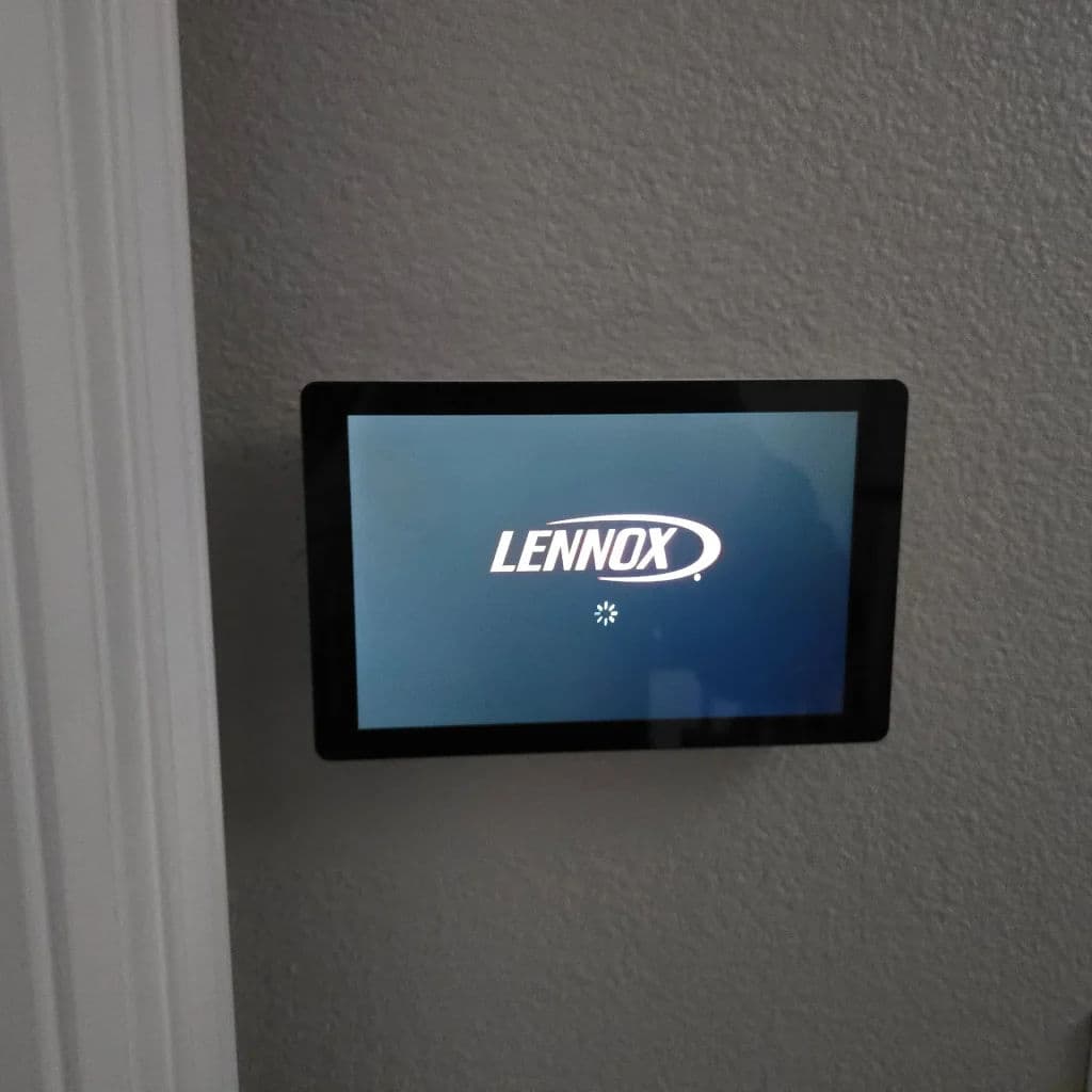Lennox smart thermostat display showing startup logo on a gray wall.