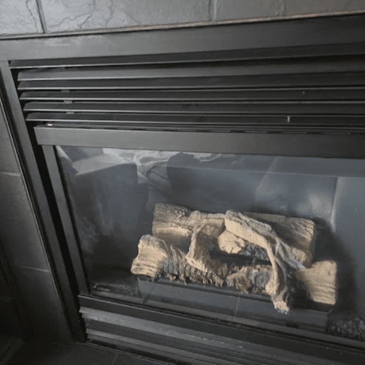 Modern fireplace with wood logs, featuring sleek black design and glass front panel.