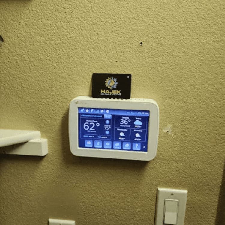 Smart thermostat displaying temperature and weather information on a beige wall.