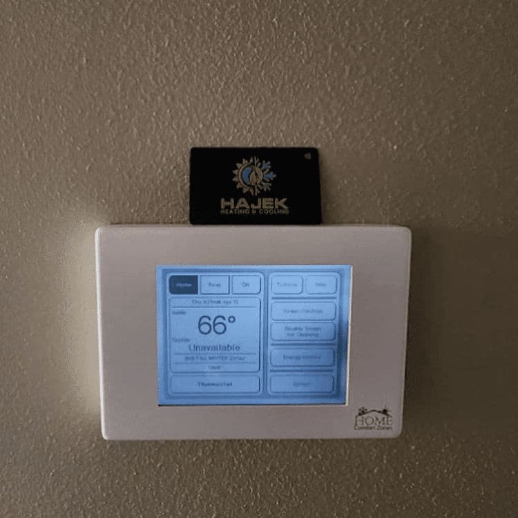 Digital thermostat displaying 66°F with Hajek Heating and Cooling business card on top.