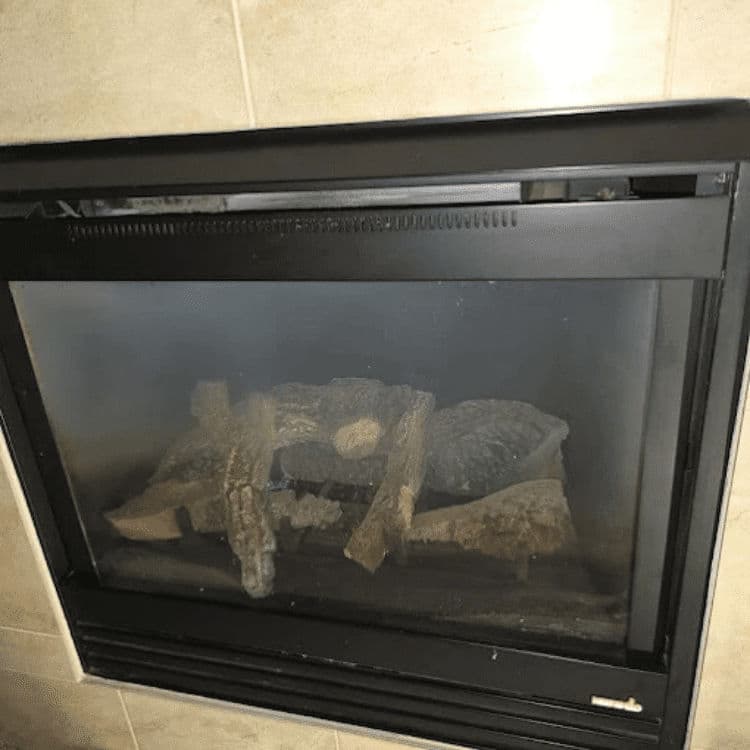 Gas fireplace with logs and glass front, set in a tiled wall background.
