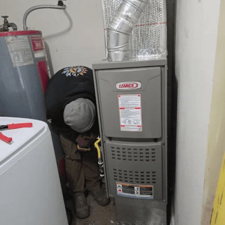 Technician servicing a Lennox furnace in a home basement with tools and equipment nearby.