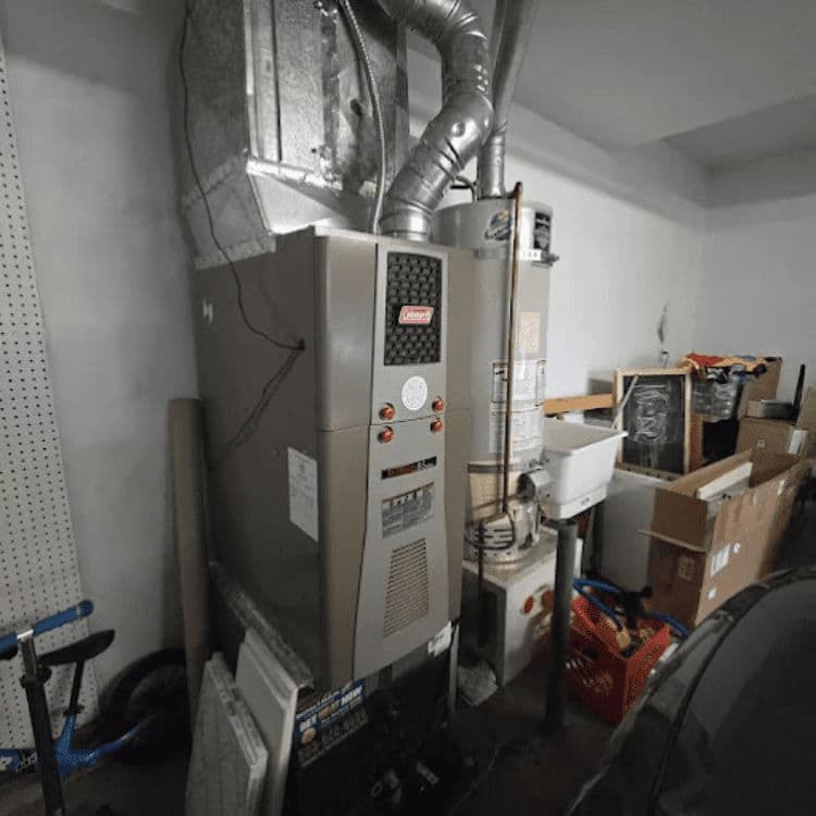 Gas furnace and water heater in a cluttered garage setting. Maintenance tools visible.