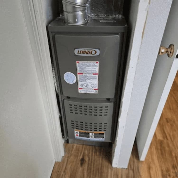 Lennox furnace installed in a narrow space beside a door on hardwood flooring.