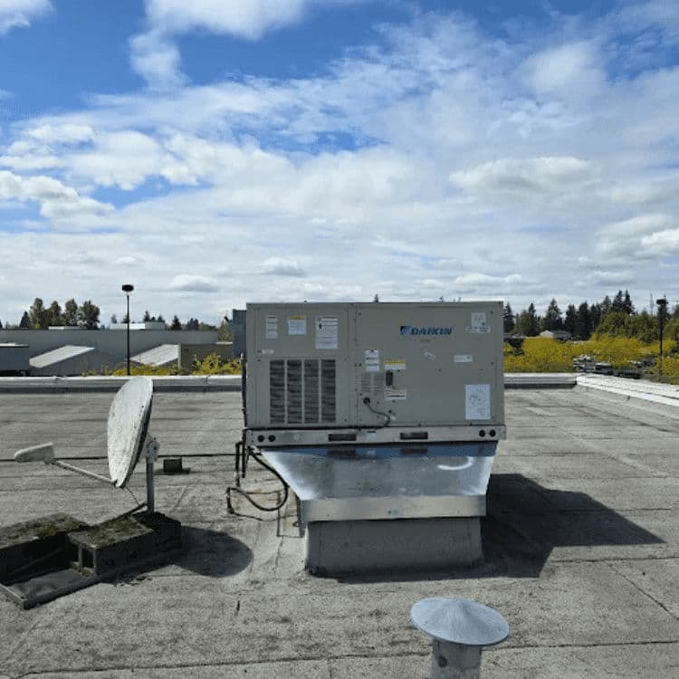 Daikin rooftop HVAC unit on flat roof under cloudy sky with satellite dish nearby.