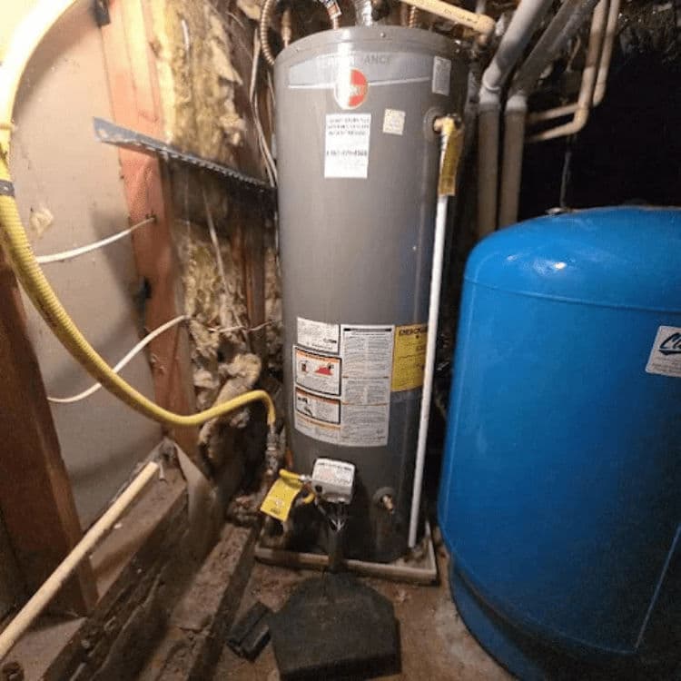 Water heater installation in a basement with a blue expansion tank and pipes.