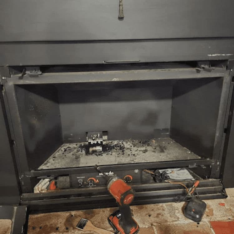 Empty fireplace with a power drill and debris on the floor, ready for home renovation.