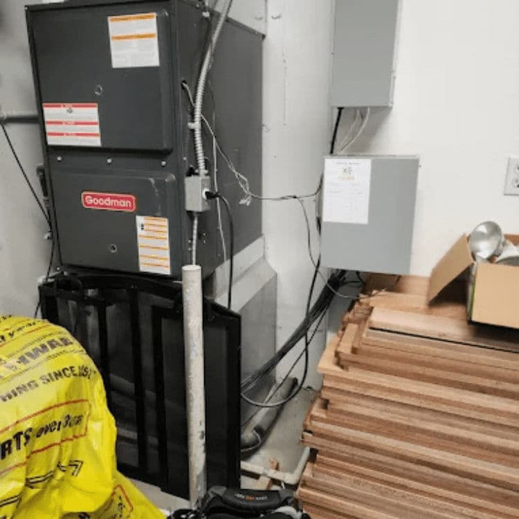 Goodman furnace in utility room with electrical panel and construction materials nearby.