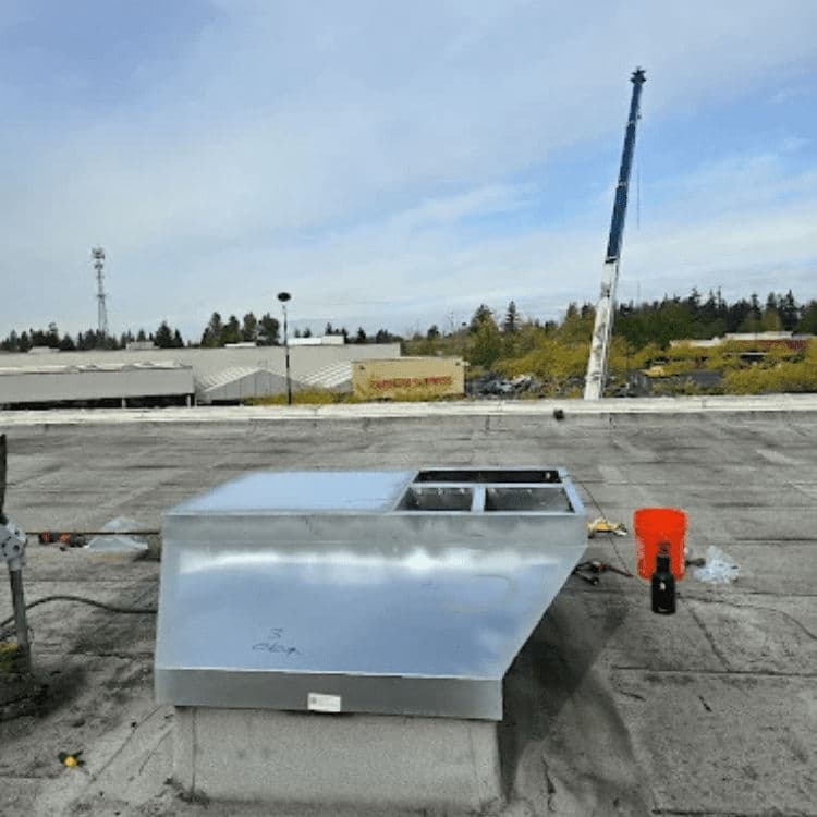 Silver rooftop ventilation unit on a commercial building with construction crane in background.