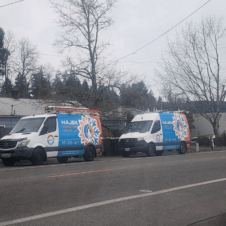 Hajek HVAC service vans parked on a residential street in winter.