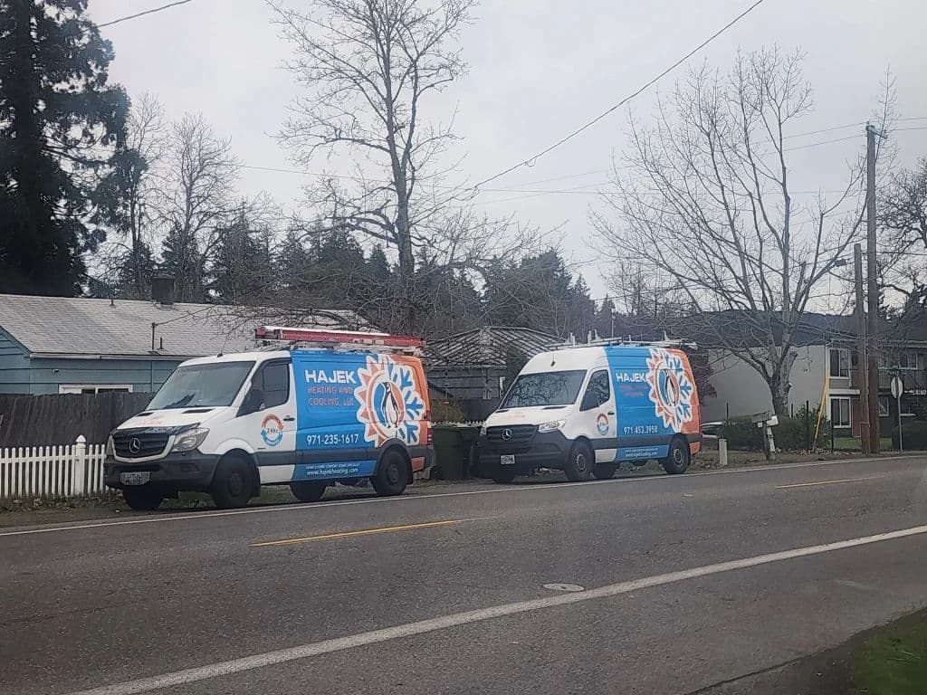 Two Haujek HVAC service vans parked on a residential street with bare trees nearby.