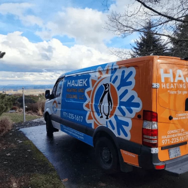 Hajek Heating and Cooling van parked outdoors with scenic background and cloudy sky.