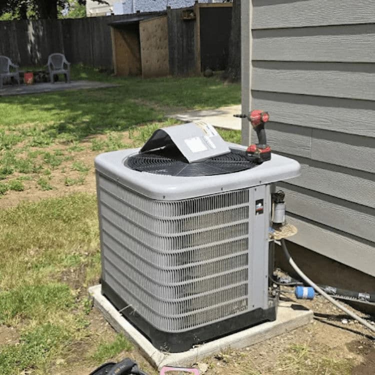 Air conditioning unit installed outside a home, with grass and fence in the background.