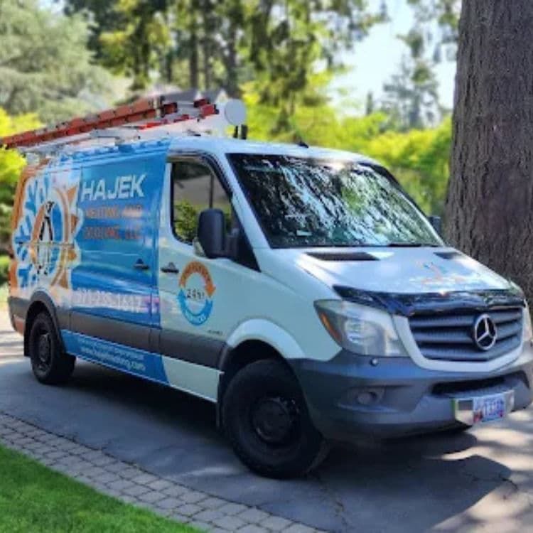 Hajek HVAC service van parked in a residential area with vibrant branding and ladder rack.